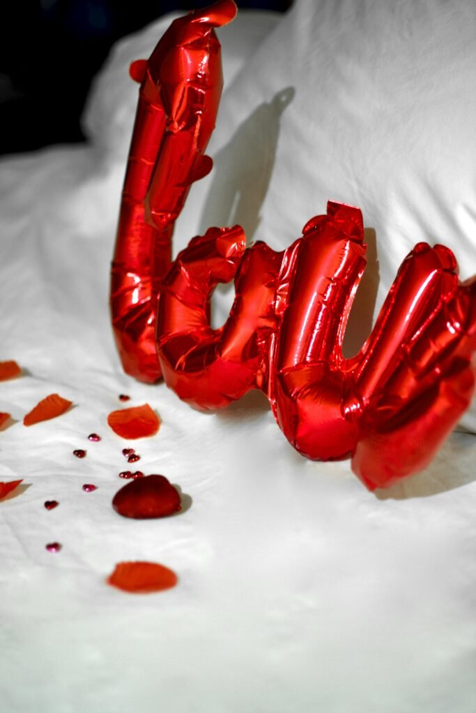 Red love balloons and rose petals on a white bed setting a romantic mood.