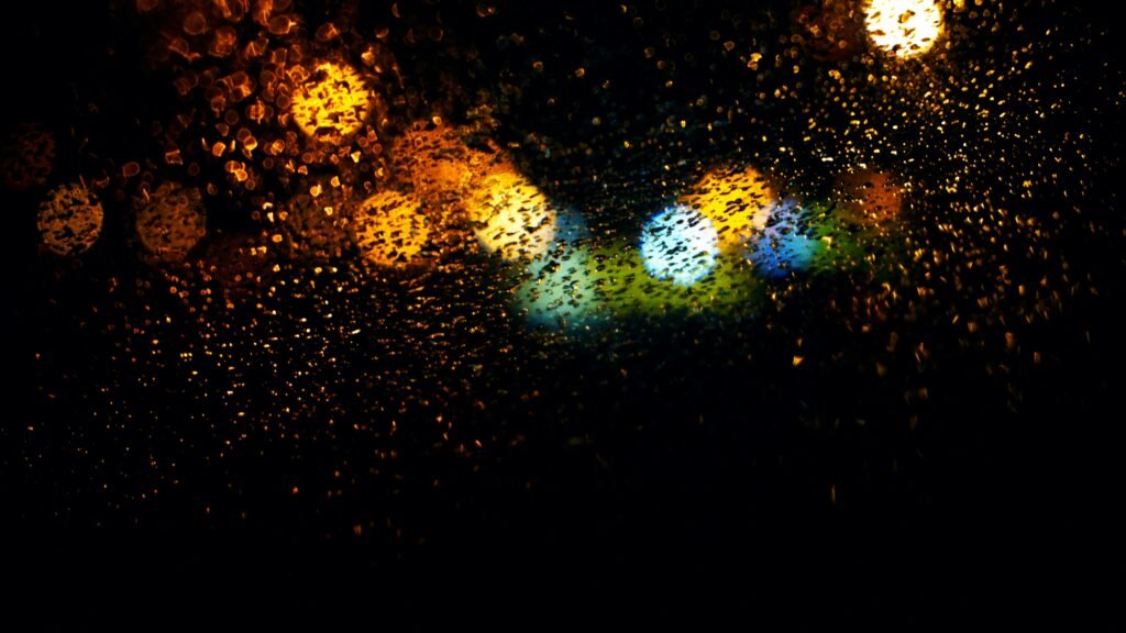 Vibrant bokeh lights on a rainy window, creating an abstract and colorful pattern.